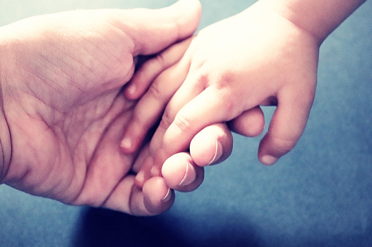 A little boy holds an adult's hand, reflecting the security and love in their relationship.